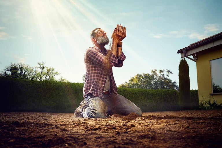 Homme agenouillé sur la terre laissant couler la terre entre ses mains, scène de jardin.