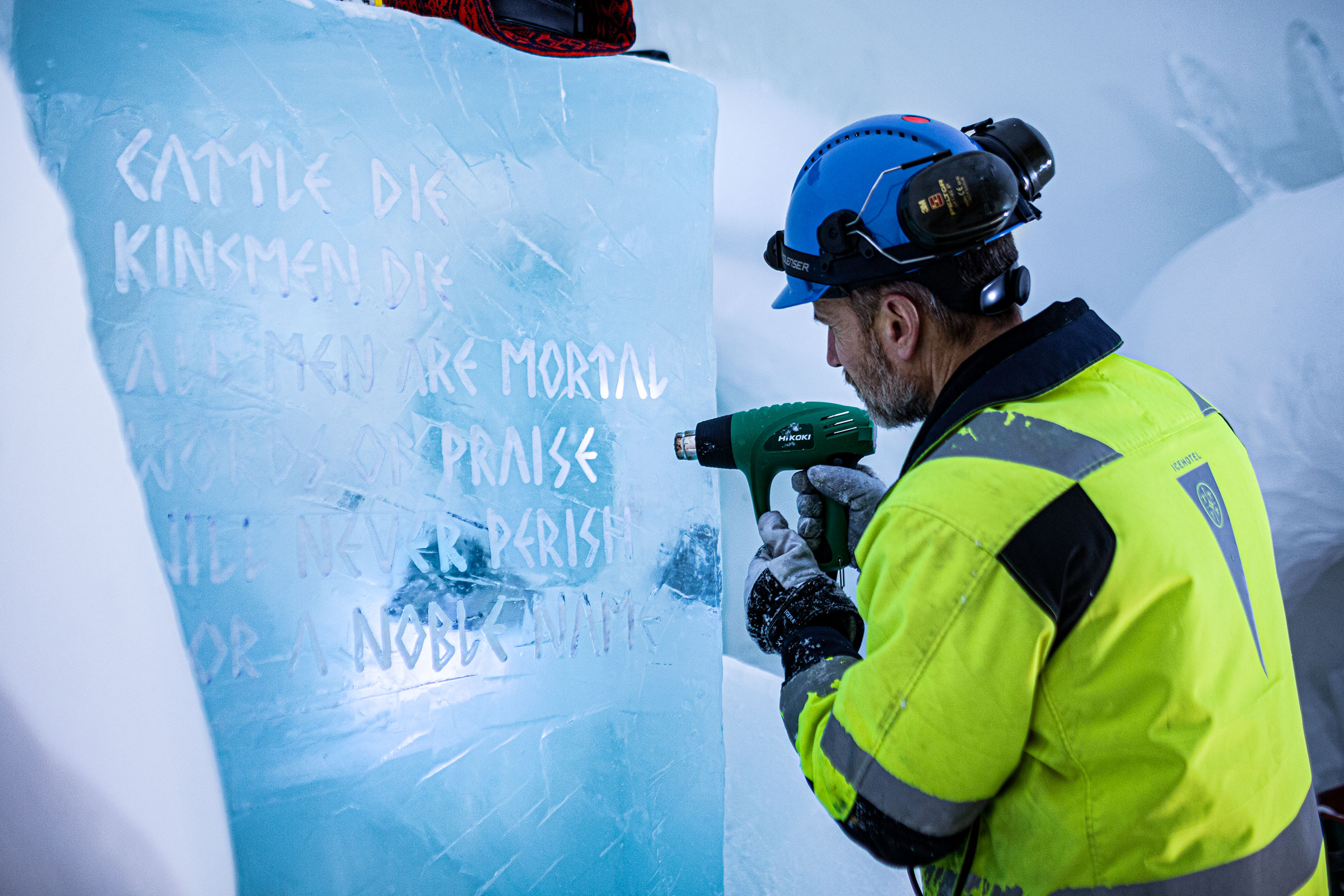 Mann graviert mit einem Heißluftgebläse einen Eisblock mit dem Text Cattle Die Kinsmen Die Allmen Are Mortal Words On Praise Niel Never Perish Or A Nobkank.