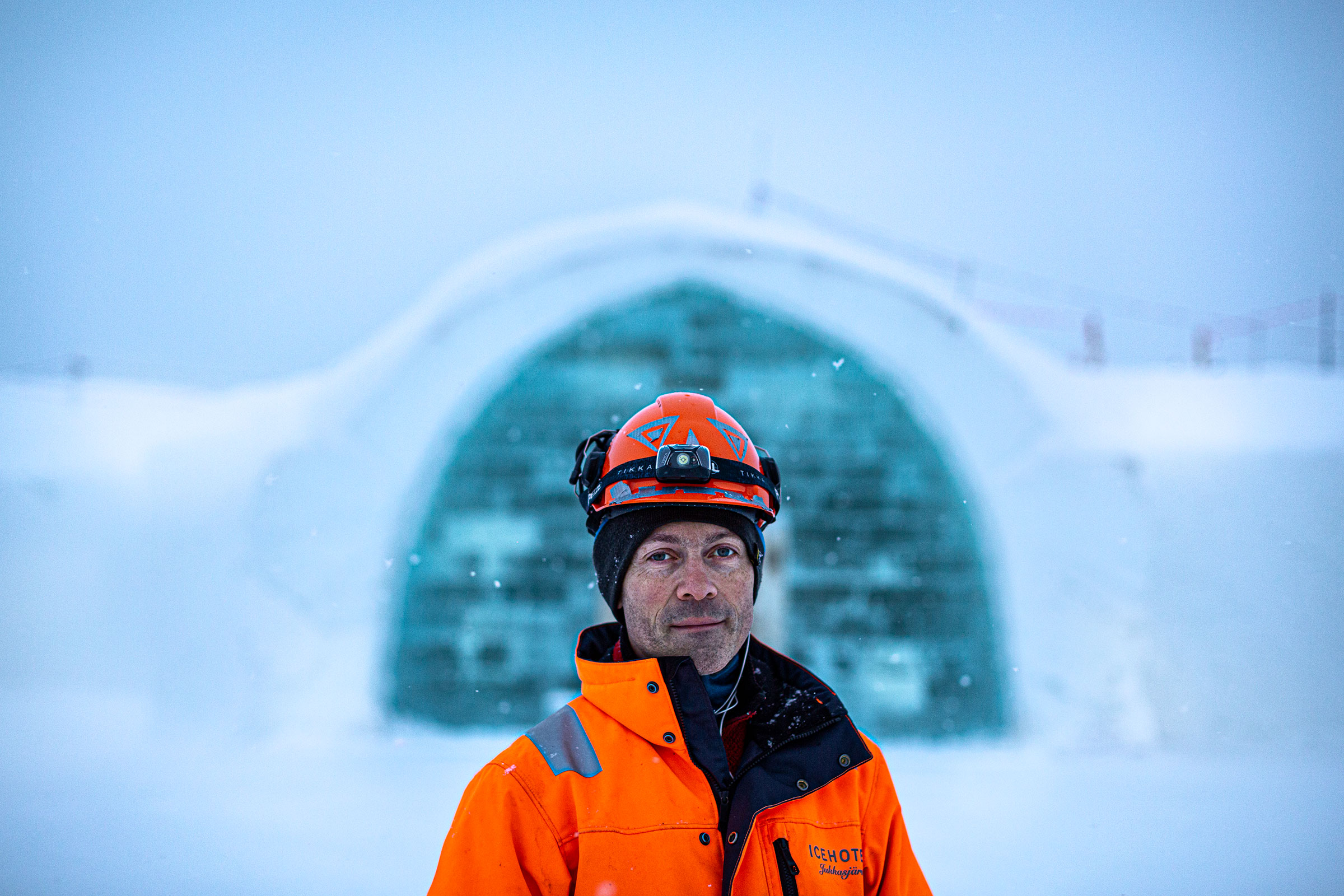 Porträt eines Mannes mit orangefarbener Jacke und Helm vor einem Eisgebäude