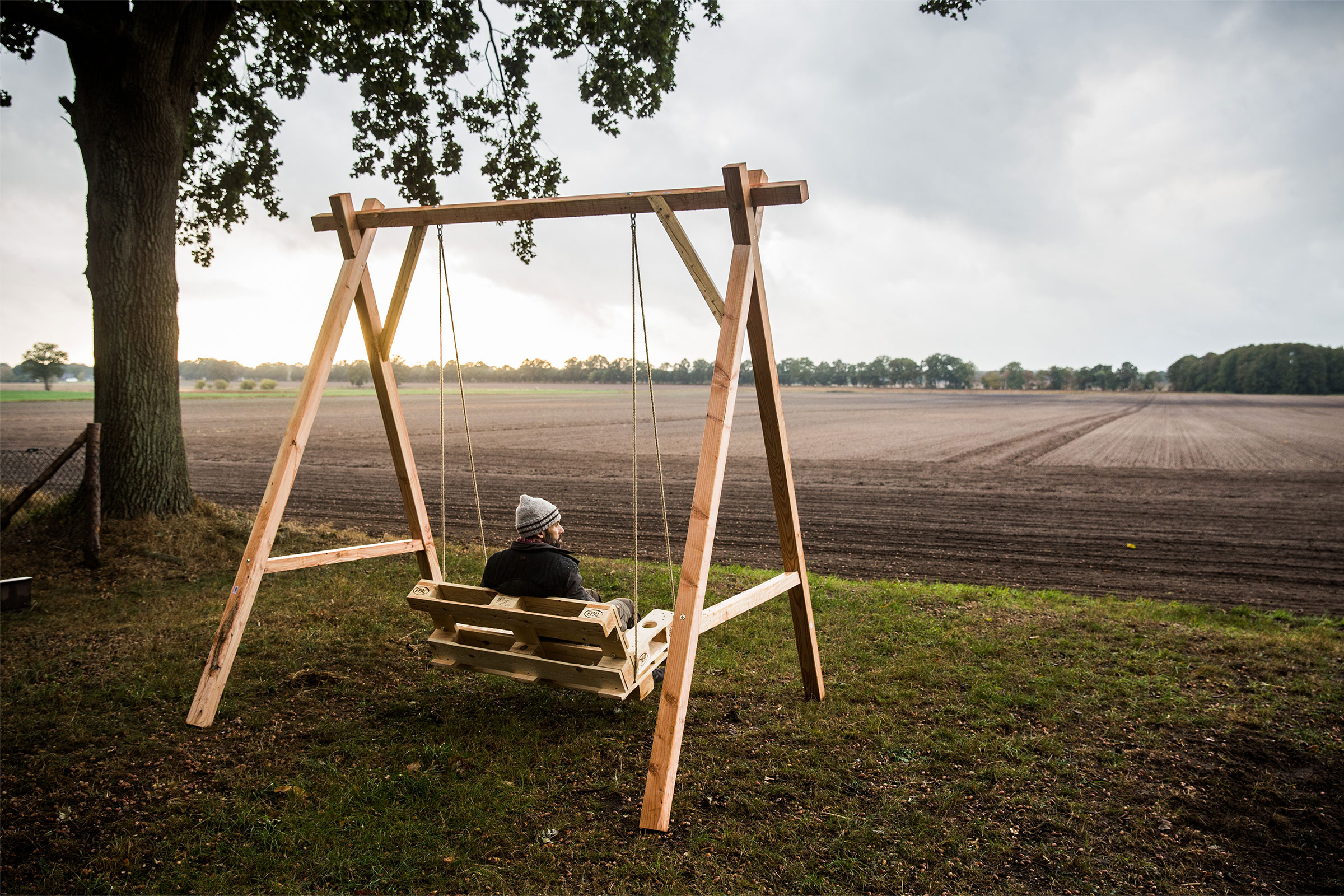 Un homme est assis sur une balançoire en bois à l'extérieur, devant un champ.