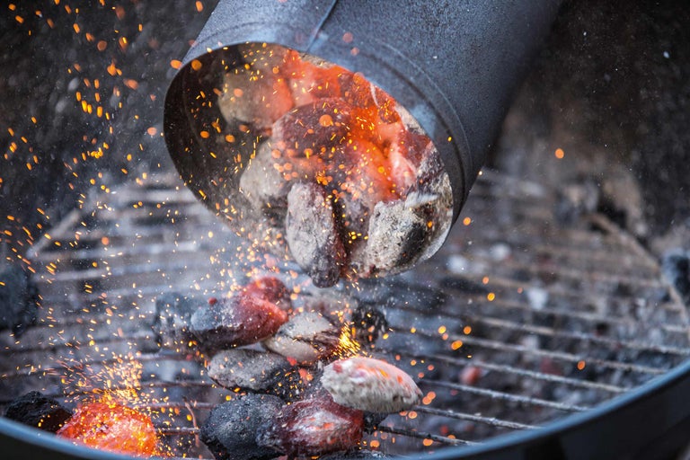 Des briquettes de barbecue incandescentes sont versées sur un gril avec une cheminée d'allumage.