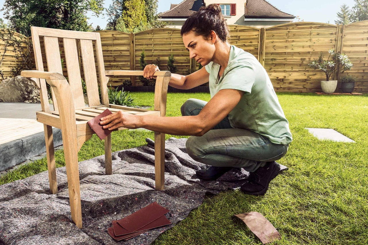 Femme ponçant une chaise en bois dans le jardin avec du papier de verre