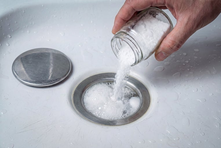 Une personne verse du bicarbonate de soude d'un bocal dans un drain.