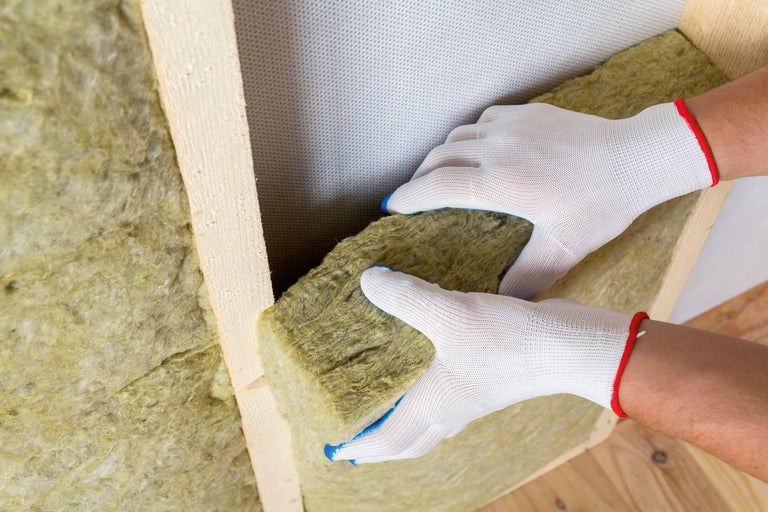 Eine Person setzt Mineralwolle zur Wärmeisolierung zwischen Holzrahmen ein.