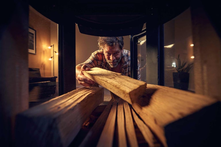 Un homme met du bois de chauffage dans un poêle à bois