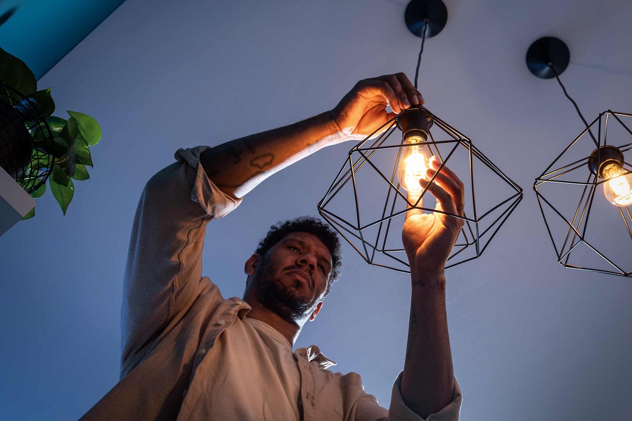 Un homme installe une ampoule LED lumineuse dans une suspension géométrique noire au design moderne.
