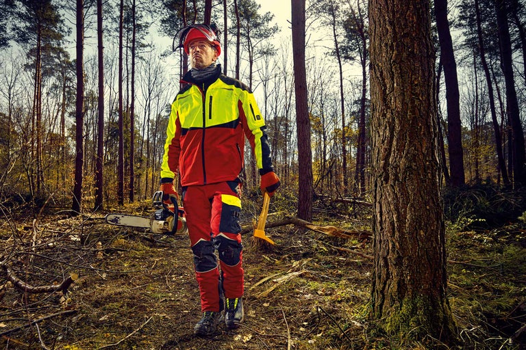 Bûcheron avec pantalon de sécurité, veste forestière, casque de protection, tronçonneuse et louchet dans la forêt