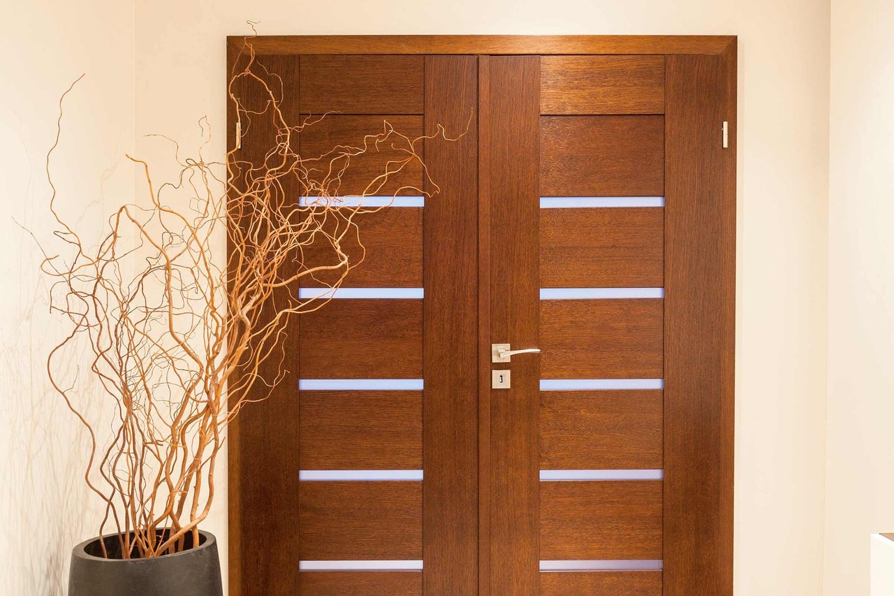Porte en bois avec inserts en verre et décoration de branches dans un pot.