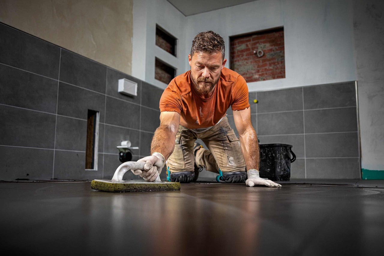Un homme joint des carreaux avec une spatule à joints dans une salle de bain.
