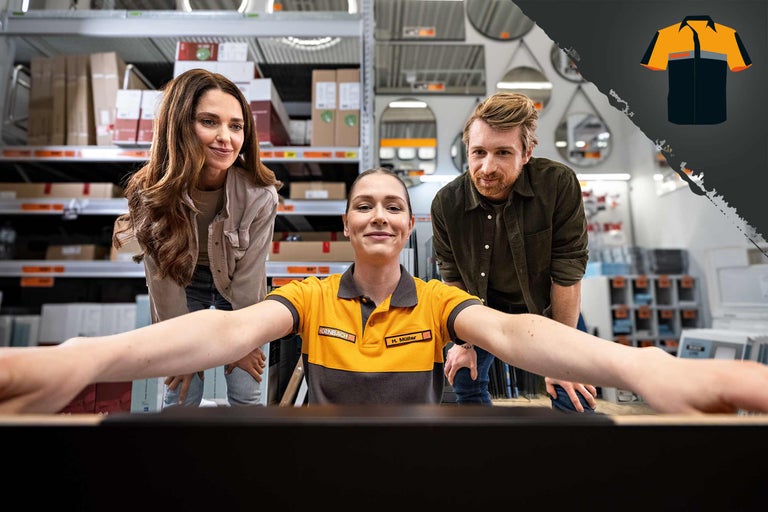 Une collaboratrice Hornbach et deux clients devant un écran dans la quincaillerie. À l'arrière-plan, des étagères avec des marchandises.