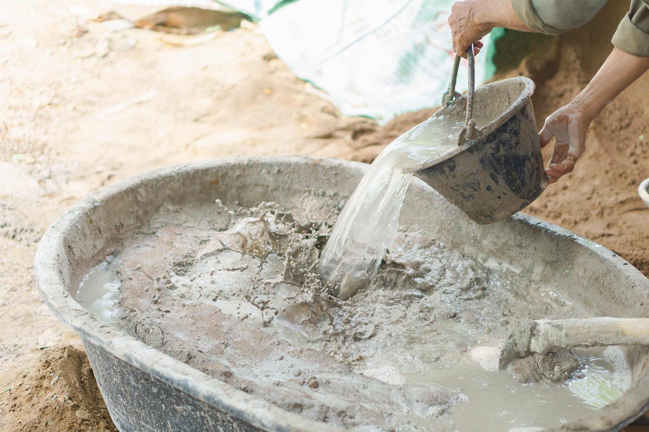Mélange de béton dans une auge à mortier avec un seau d'eau.