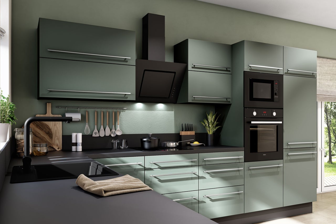 Cuisine équipée moderne vert mat avec plan de travail noir, four, micro-ondes, hotte et poignées argentées.