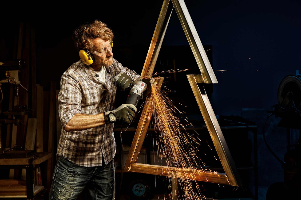 Un homme meule une construction métallique avec une meuleuse d'angle, des étincelles volent.