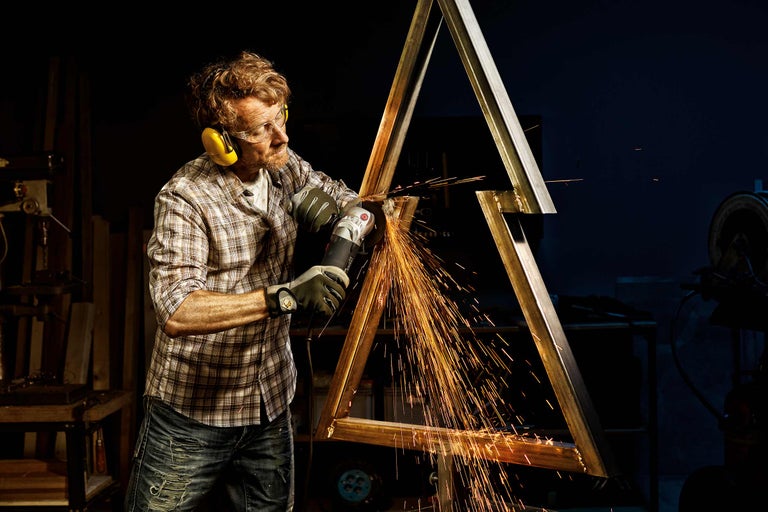 Un homme meule une construction métallique avec une meuleuse d'angle, des étincelles volent.