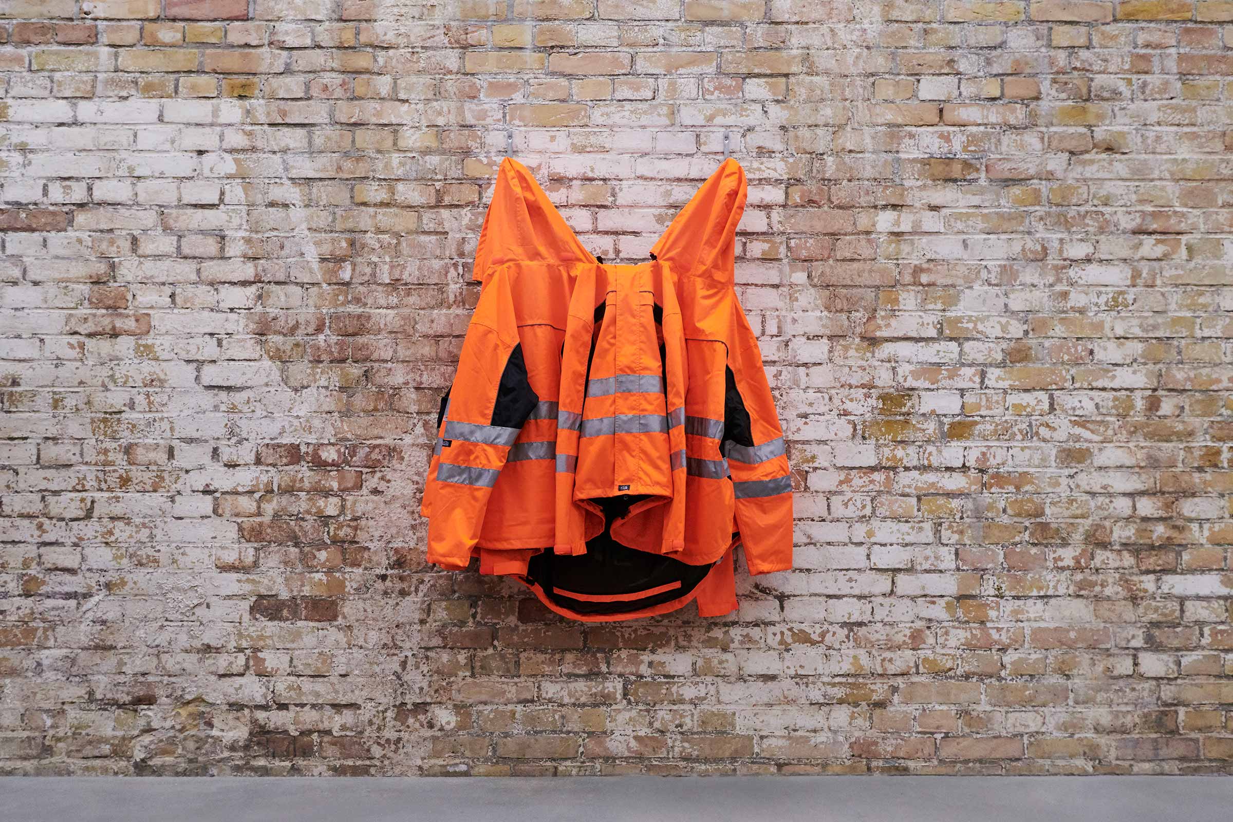 Orangefarbene Warnjacke mit Reflektorstreifen an einer Ziegelwand