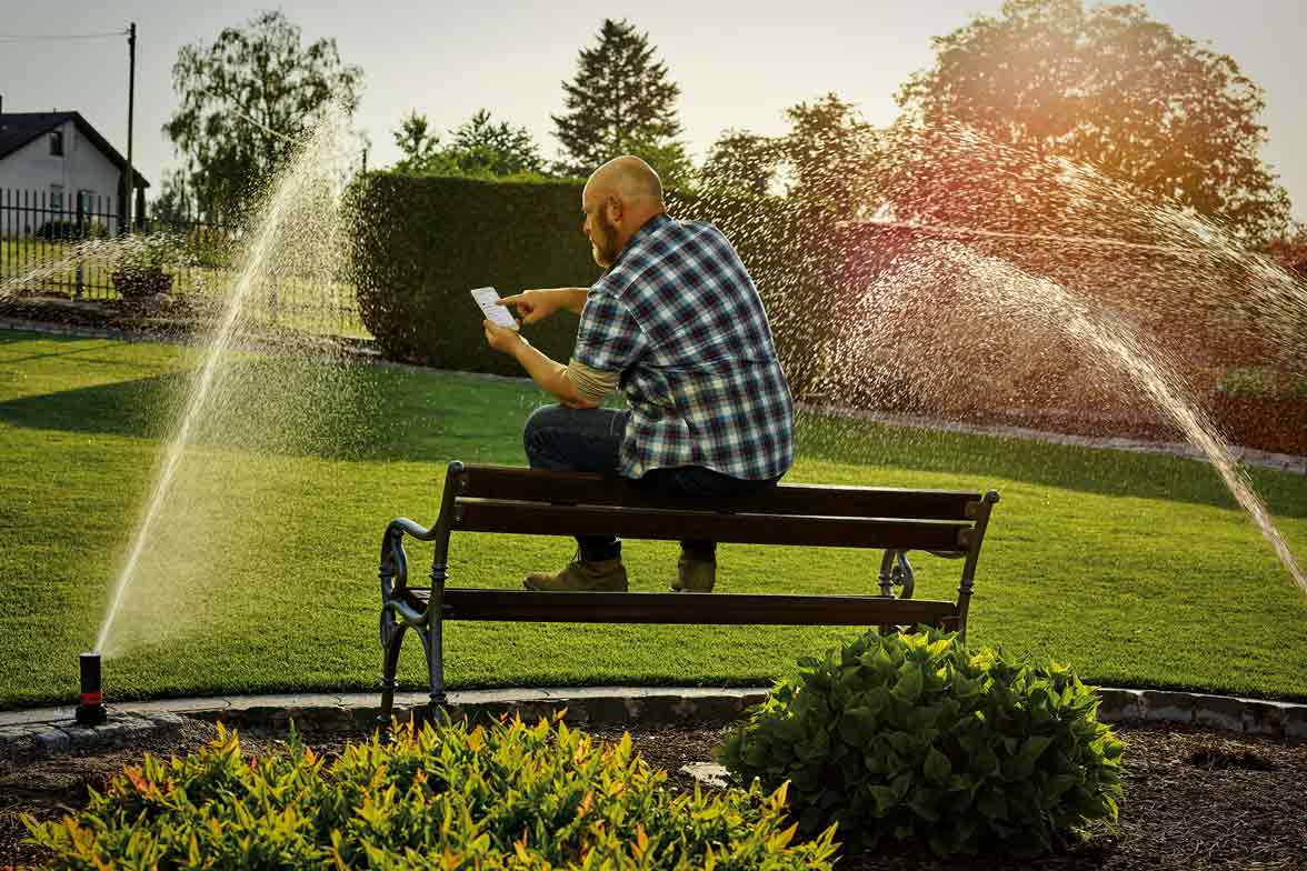 Un homme est assis sur un banc et utilise son smartphone pour commander un système d'irrigation