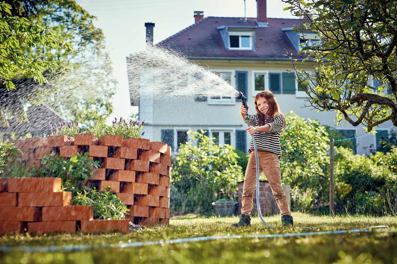 Une fille arrose des plantes dans un jardin avec un tuyau d'arrosage et un pistolet d'arrosage.