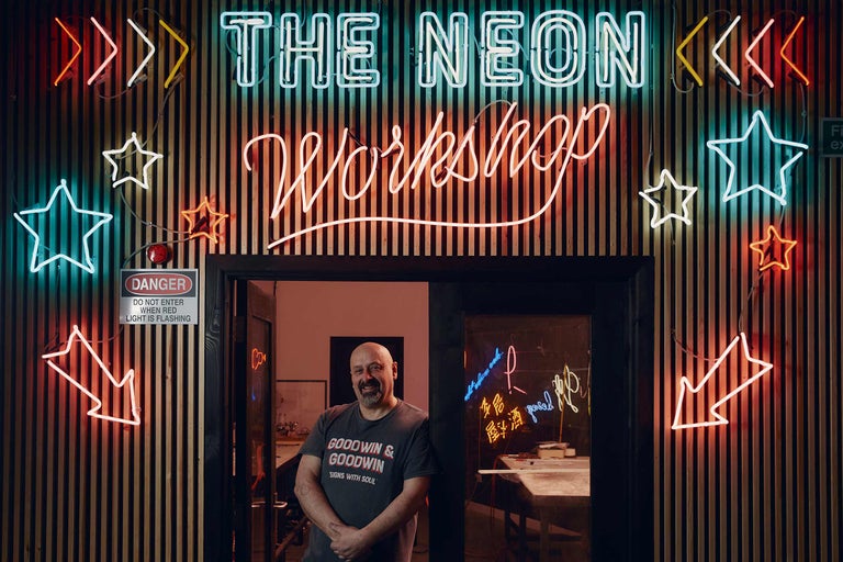 Eingang zu The Neon Workshop mit Neonreklamen und einem Warnschild