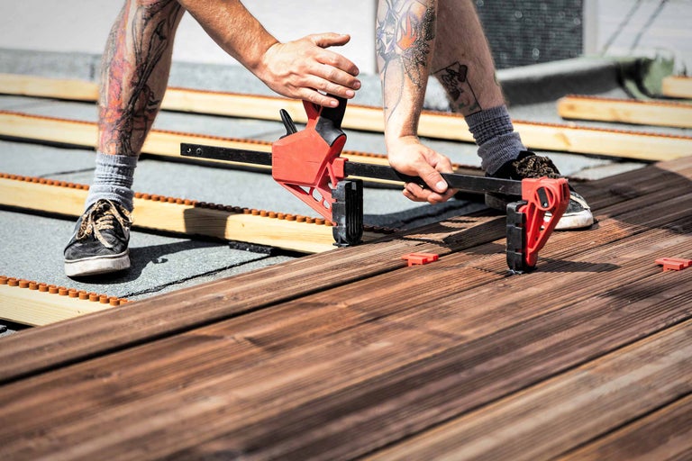 Un homme pose une terrasse en bois avec un serre-joint