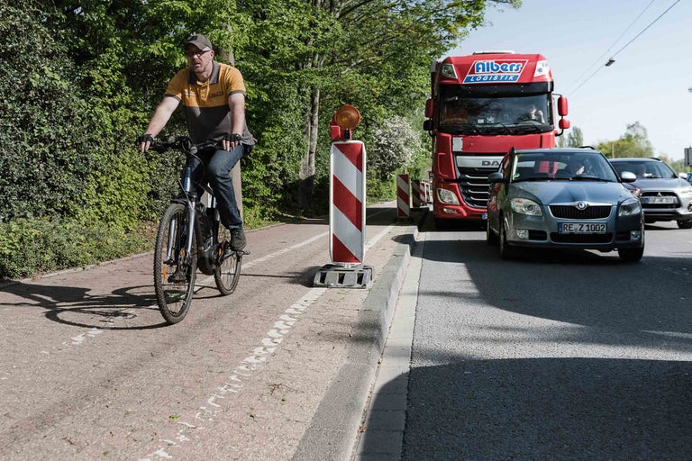 Radfahrer auf Radweg mit rot-weißen Warnbaken und Straßenverkehr
