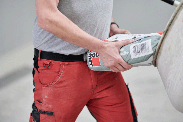 Un homme en pantalon de travail verse un sac de ciment de construction dans une brouette