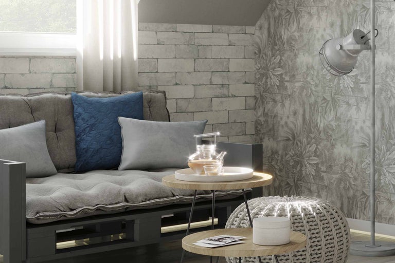 Wohnzimmer mit Palettensofa, Kissen, Beistelltischen, Strickhocker und Stehlampe vor gemusterter Tapete