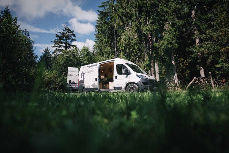 Une camionnette blanche avec l'inscription BUILDIFY garée dans la forêt, la porte est ouverte.