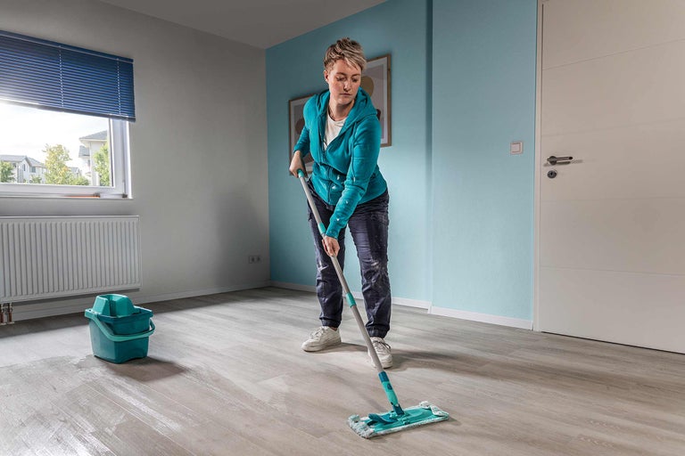 Femme nettoie le sol avec une serpillère dans une pièce avec un seau et un radiateur