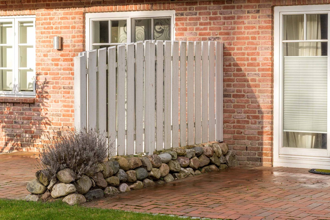 Clôture de protection visuelle en bois avec mur de pierre devant une maison en briques