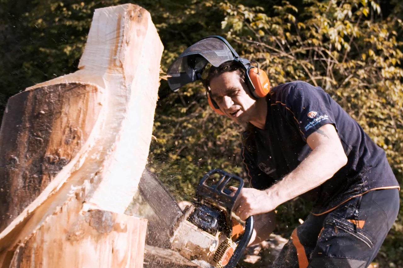 Mann mit Kettensäge beim Holzbearbeiten mit Sicherheitsausrüstung