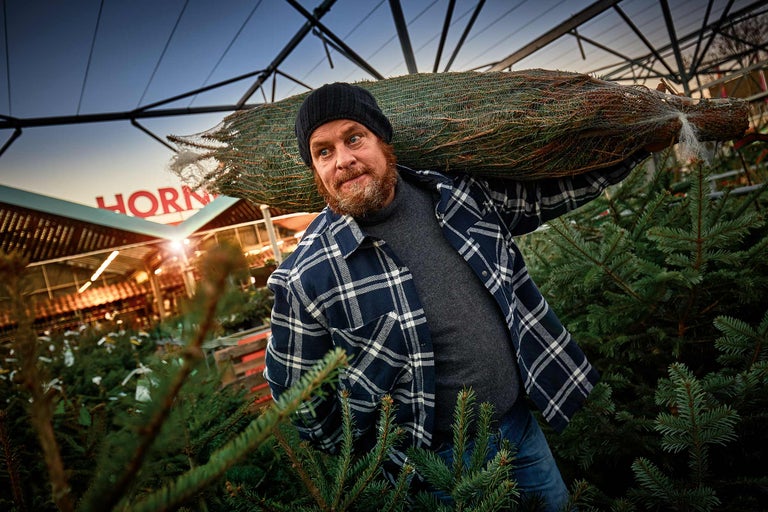 Un homme porte un sapin de Noël emballé sur l'épaule dans un magasin Hornbach.
