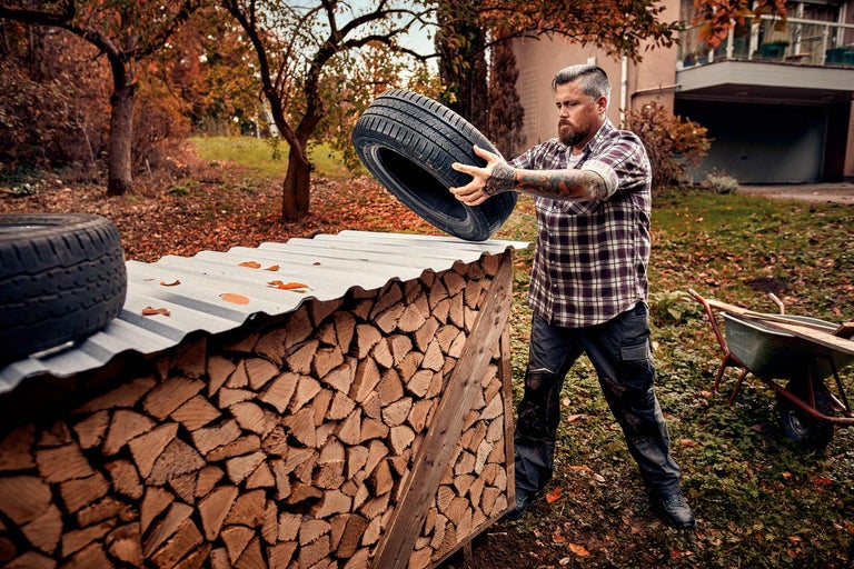 Un homme entrepose des pneus sur une pile de bois dans le jardin.
