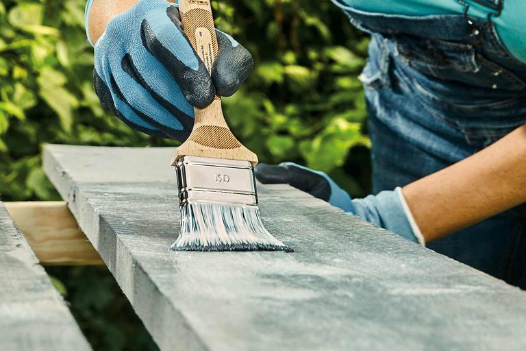 Une personne peint une planche de bois avec un pinceau.