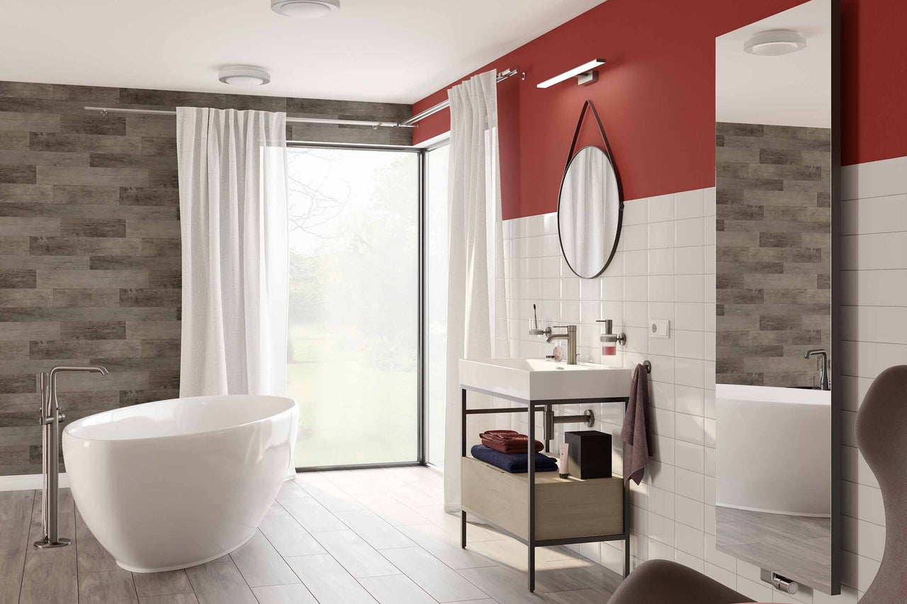 Salle de bains avec baignoire îlot, lavabo, miroir et grande fenêtre.