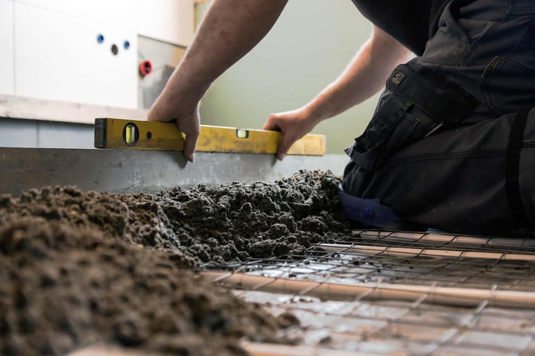 Ein Handwerker nivelliert Estrich mit einer Wasserwaage auf einer Baustelle.