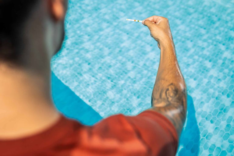 Un homme vérifie la qualité de l'eau avec des bandelettes de test pour piscine.