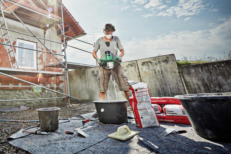 Handwerker mischt Zement mit einem elektrischen Rührer auf einer Baustelle.