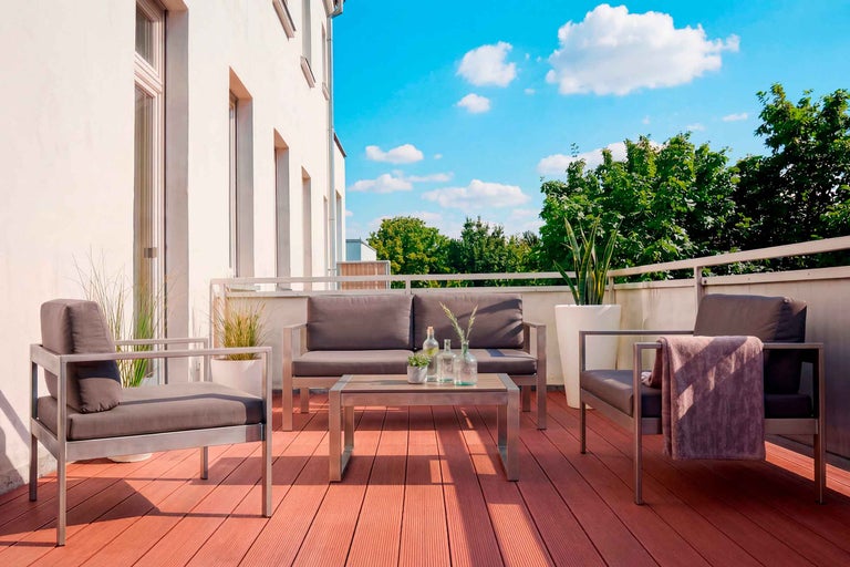 Modernes Lounge-Set aus Metall mit grauen Polstern auf einer Terrasse mit WPC-Dielen, bestehend aus Sofa, Sesseln und Tisch.