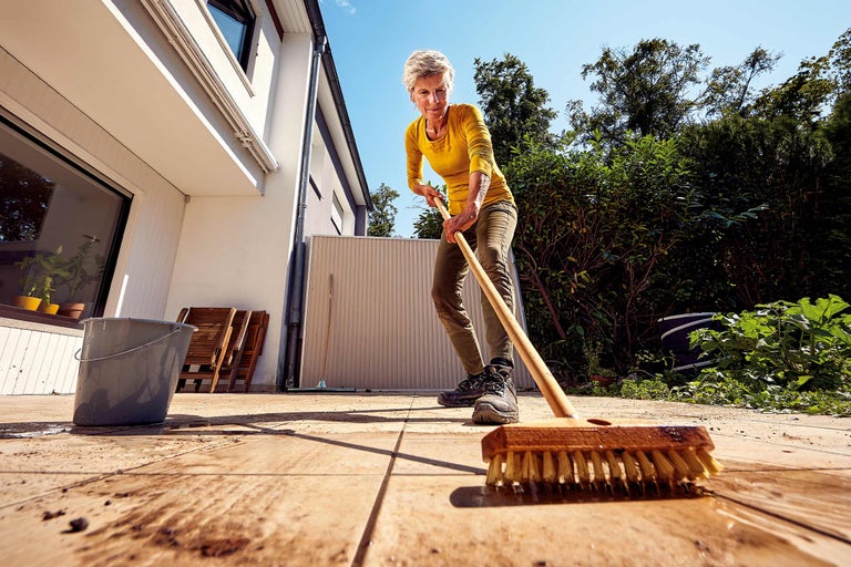 Femme nettoie terrasse avec une brosse