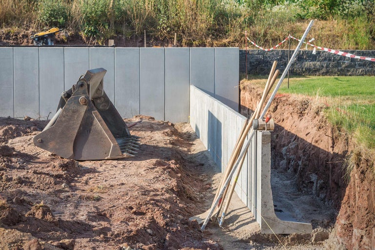 Travaux de construction avec mur en béton, godet d'excavatrice et outils dans une fosse de construction.