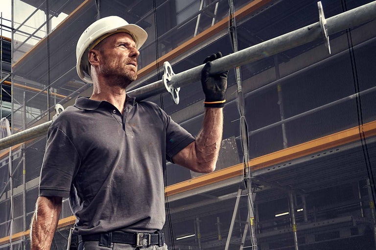 Ouvrier du bâtiment avec casque de protection portant une barre d'échafaudage devant un échafaudage