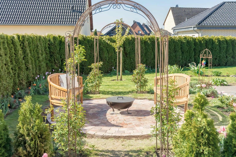 Scène de jardin avec arche de roses, bancs et brasero sur un sol pavé