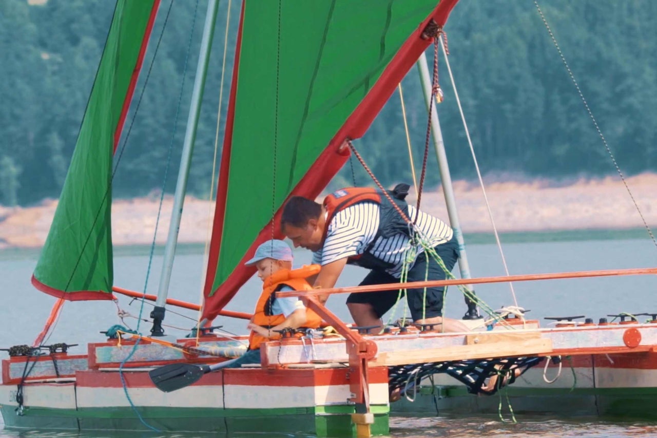 Homme et enfant avec gilets de sauvetage sur voilier.