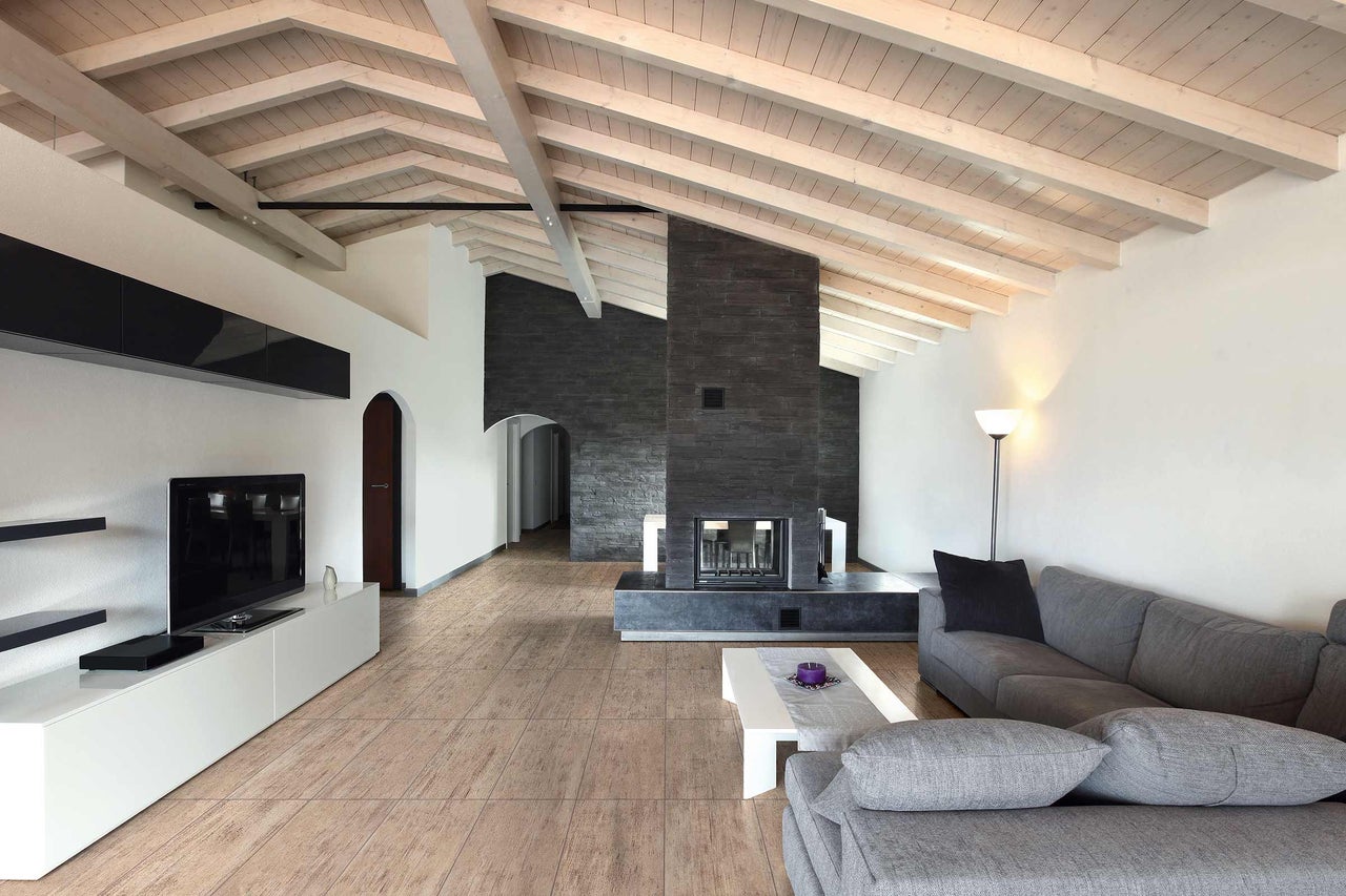 Salon avec cheminée, canapé gris et plafond à poutres apparentes