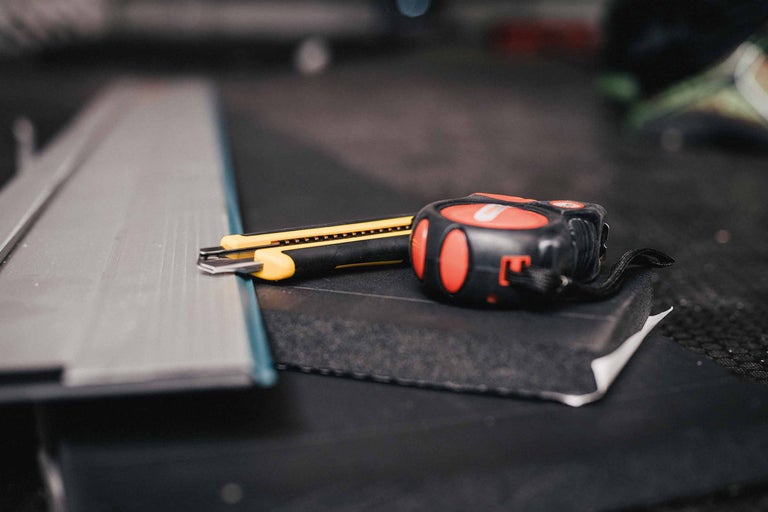 Metallprofil, Cuttermesser und Rollbandmass liegen auf einer Oberfläche