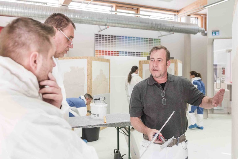 Innenaufnahme einer Schulung für Stuckateure mit einem Kursleiter und Teilnehmern in Arbeitskleidung