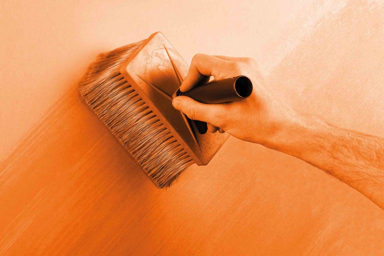 Une personne peint un mur avec une brosse plate.