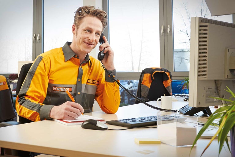Un collaborateur Hornbach téléphone et prend des notes à son bureau.