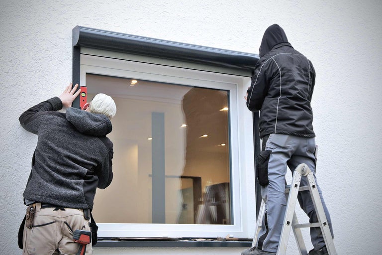 Deux installateurs installent un volet roulant sur une fenêtre.