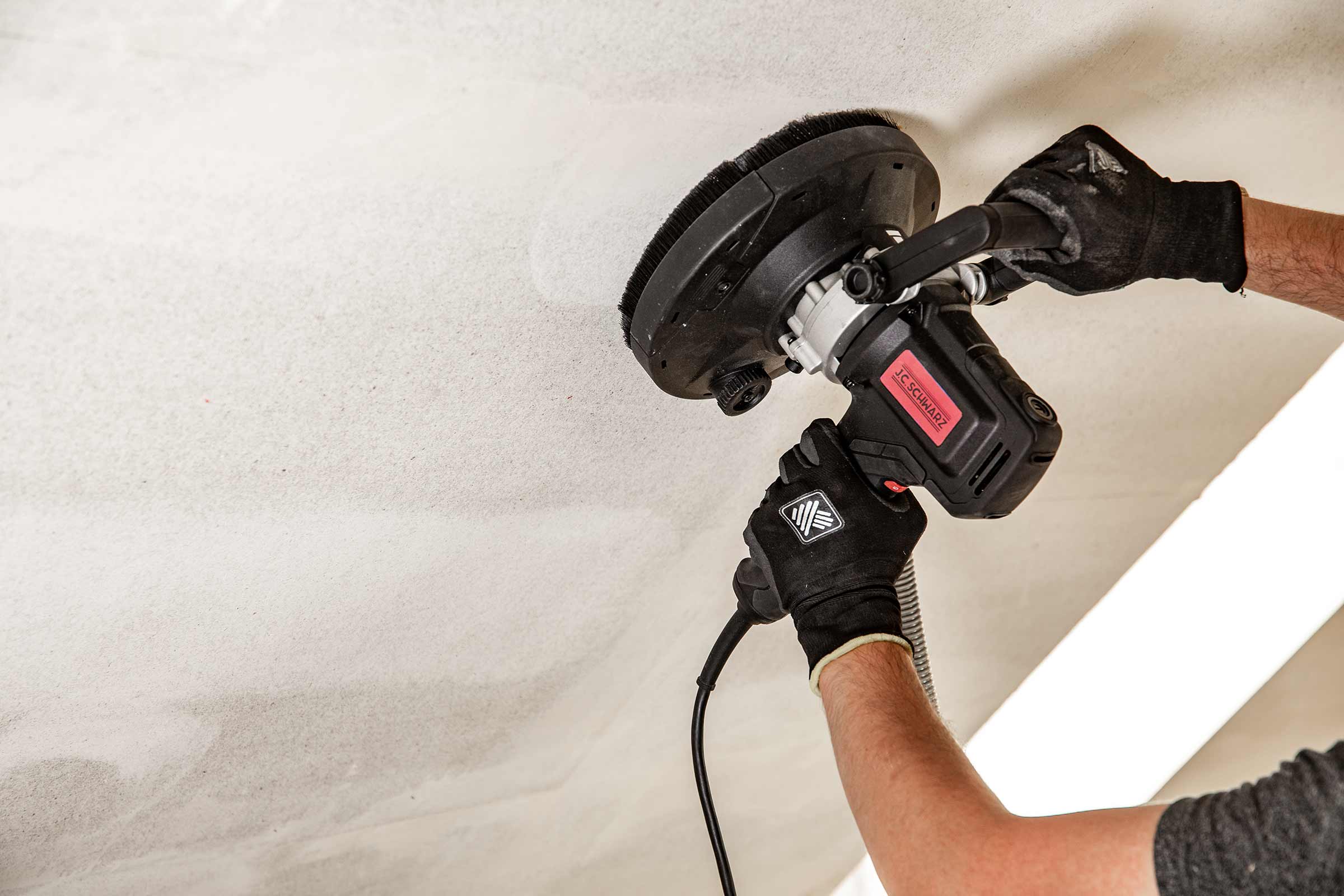 Un artisan utilise une ponceuse à plafond JC Schwarz pour travailler un plafond.